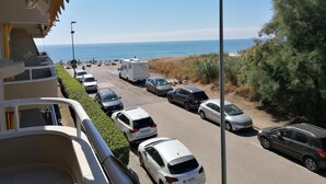 Un espace de stationnement avec plusieurs voitures et une caravane, offrant une vue sur une plage et la mer.