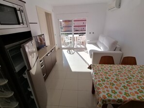 Eine moderne Küche mit Mikrowelle, Backofen und Spüle. Ein Essbereich mit Tisch und Stühlen sowie ein weißes Sofa sind ebenfalls vorhanden.