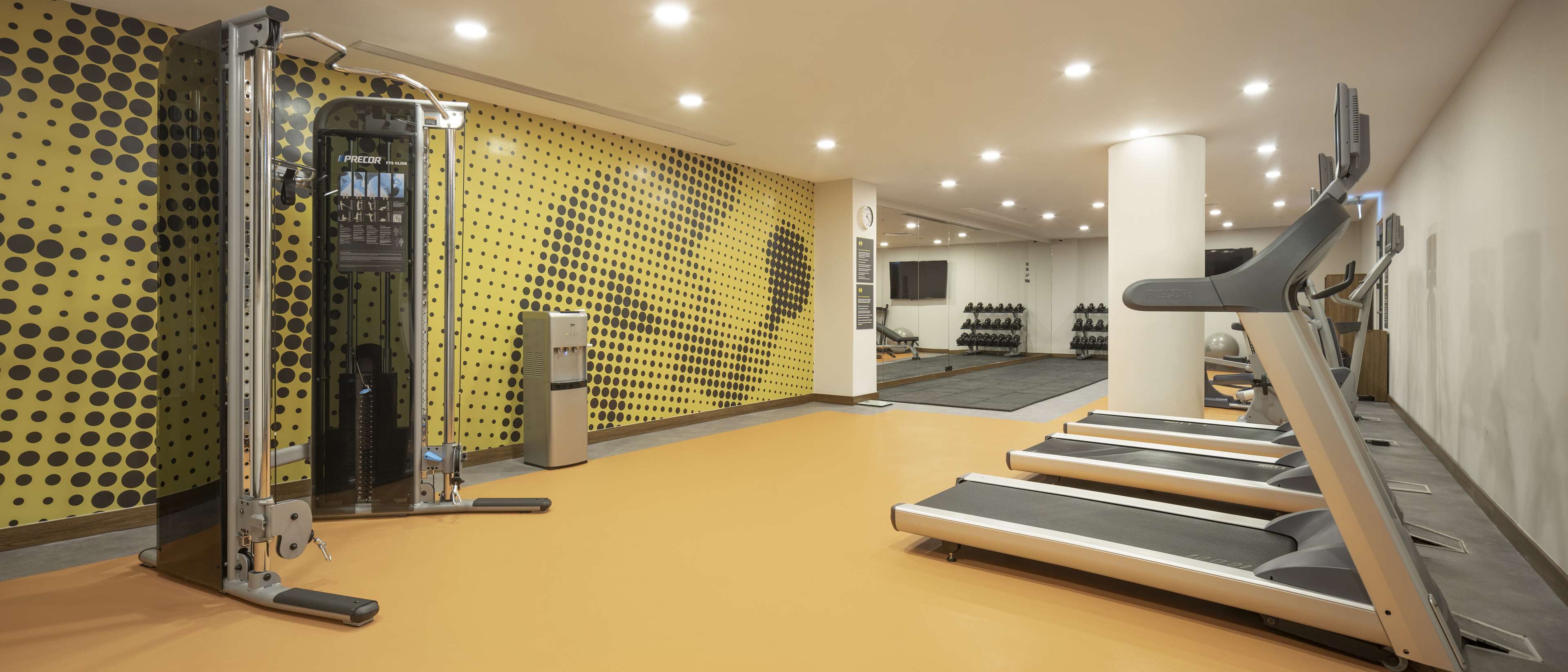 Ein Fitnessraum mit Laufbändern, einem Wasserspender und einer Wand mit Punkte-Muster.