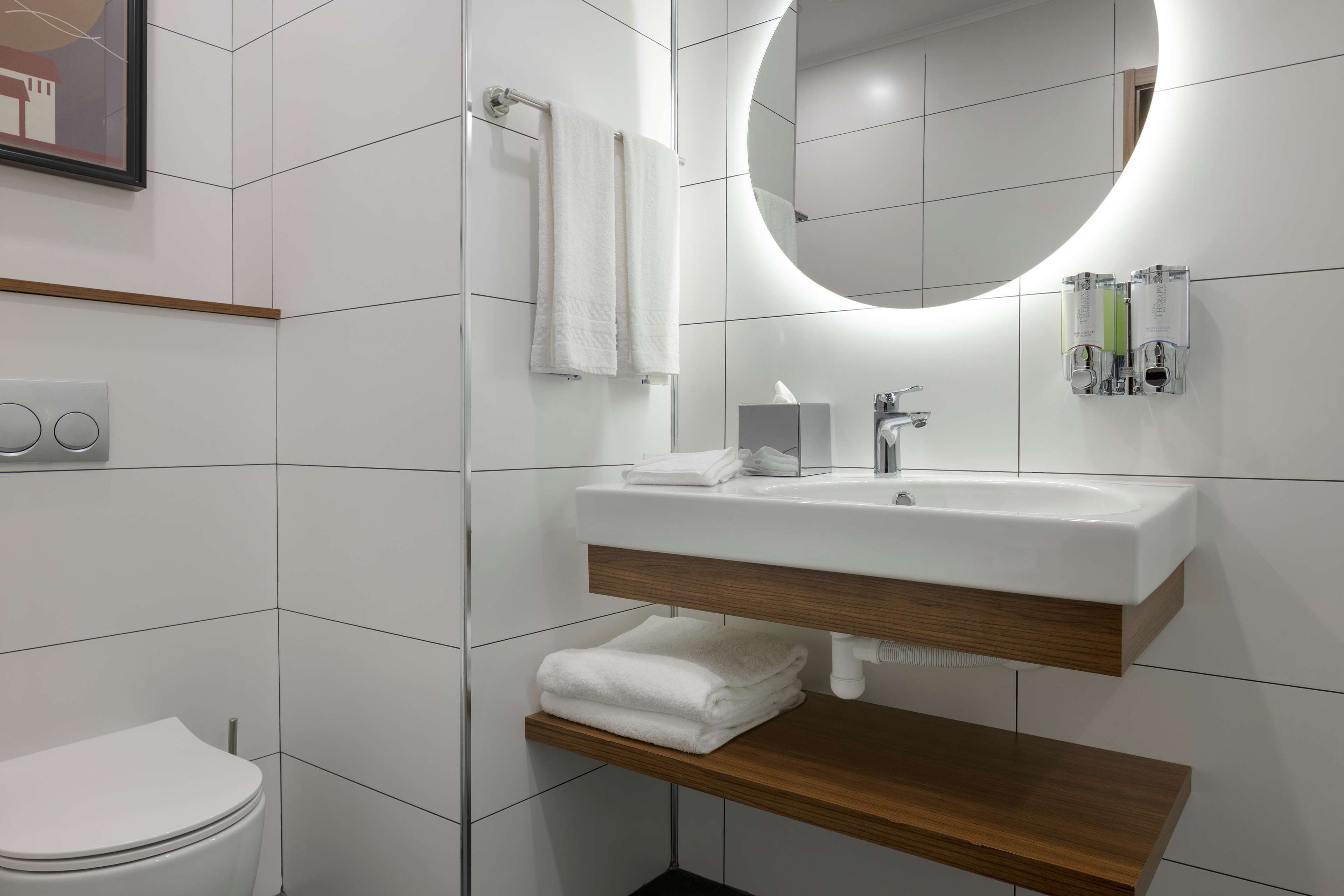 A modern bathroom with a white sink, wooden vanity, and a large mirror.