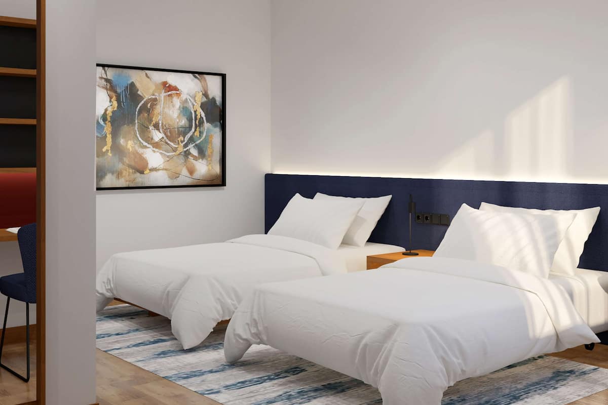 Ein modernes Hotelzimmer mit zwei Betten, einem blauen Kopfteil, Holzboden und einem großen, abstrakten Gemälde an der Wand.