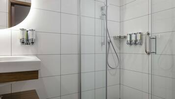 Une salle de bain moderne avec une douche à parois de verre, des murs recouverts de carreaux blancs et un meuble-lavabo en bois.