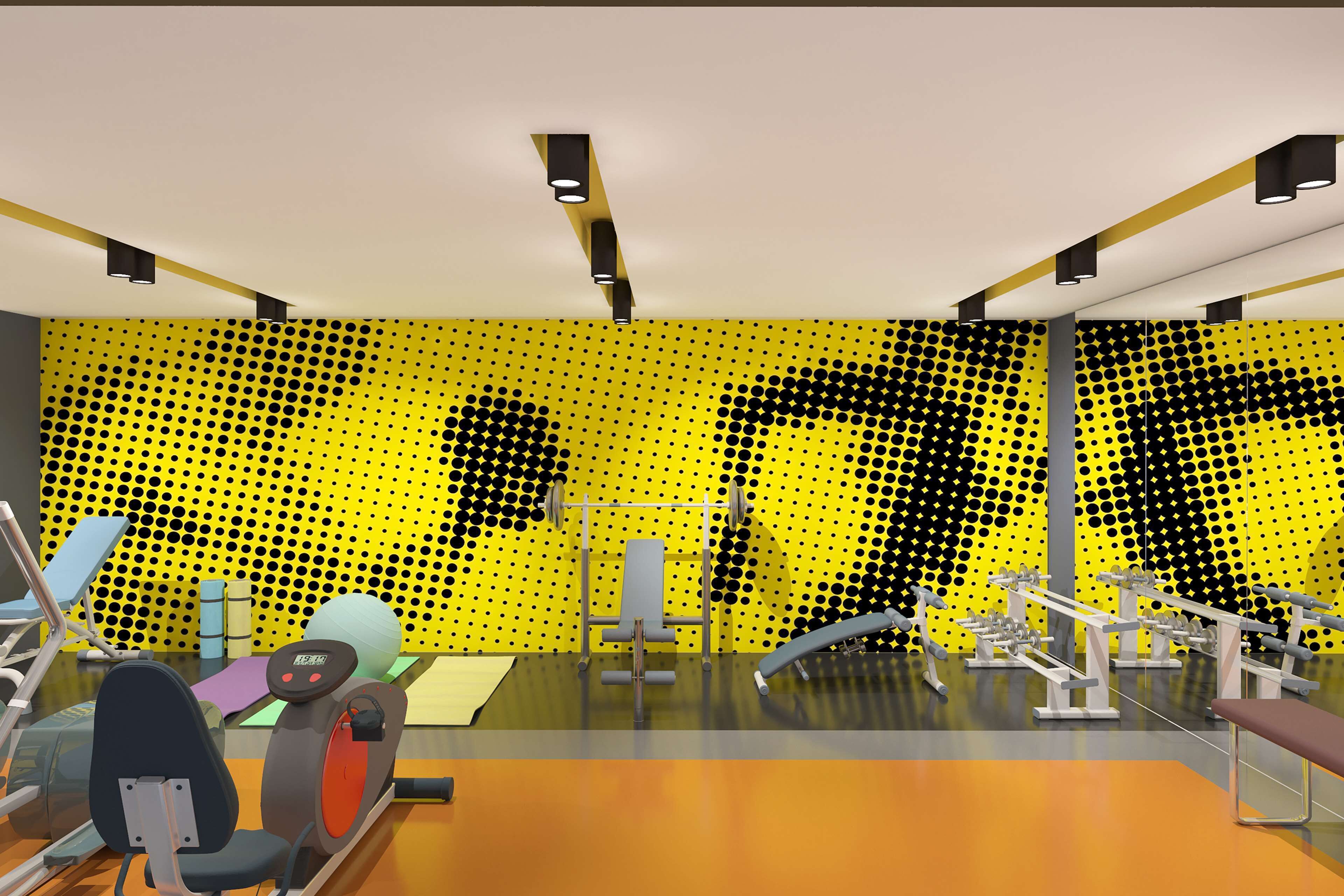 A modern gym with various exercise equipment, a yellow patterned wall, and a large mirror.