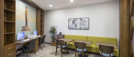 A modern office space with a wooden desk, computer, and chairs. There is a yellow sofa and a plant in the corner.