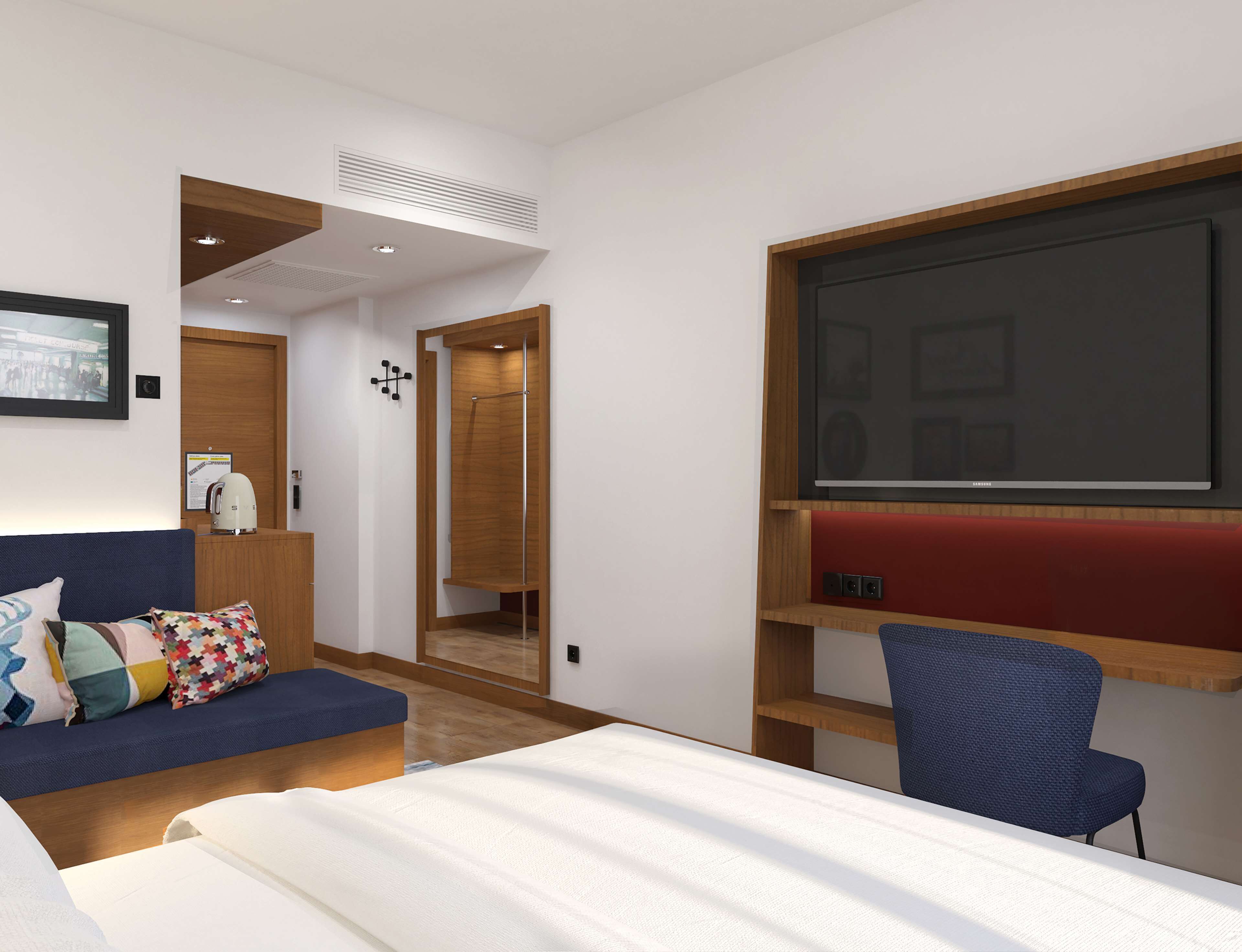 A modern hotel room with a bed, a blue sofa, a desk with a chair, a large TV, and a wooden wardrobe.