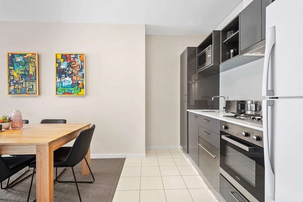 Una cocina moderna con comedor, que incluye una mesa de madera, sillas y dos cuadros abstractos de colores en la pared.