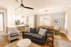 A spacious living room with a gray sofa, a round coffee table, and a dining area with a wooden table and chairs.
