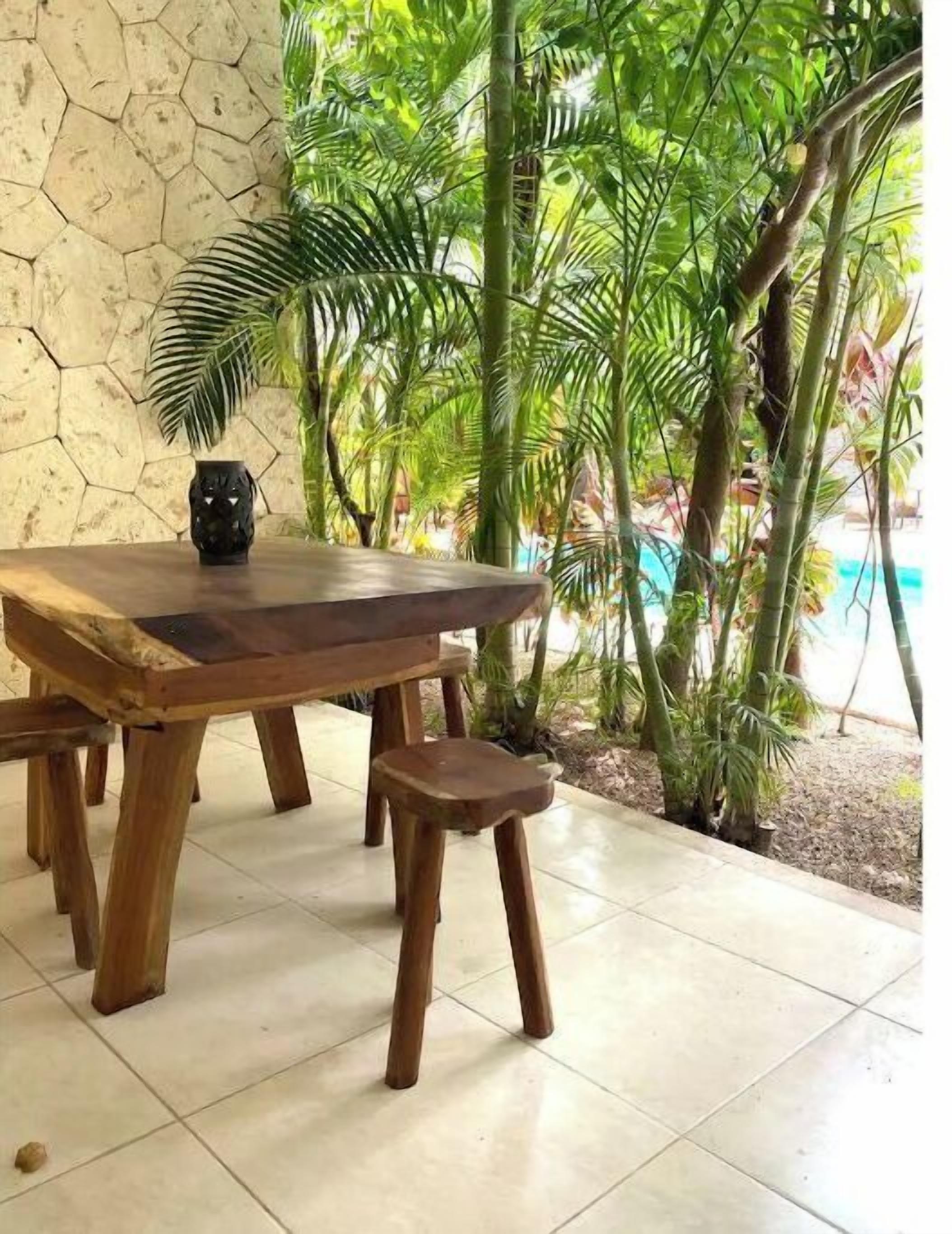 A wooden table with a bench in a room with a stone wall and tropical plants.
