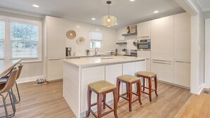 A modern kitchen with a large island, white cabinetry, and three wooden stools. - Covered patio, fenced back yard, open floor plan (North Charleston)