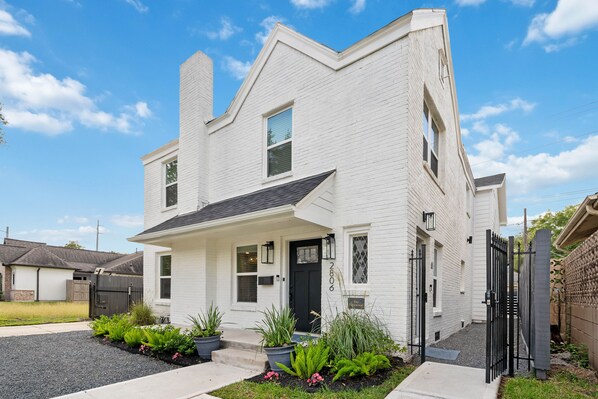 A two-story white house with a black front door, a small front porch, and a gravel driveway.