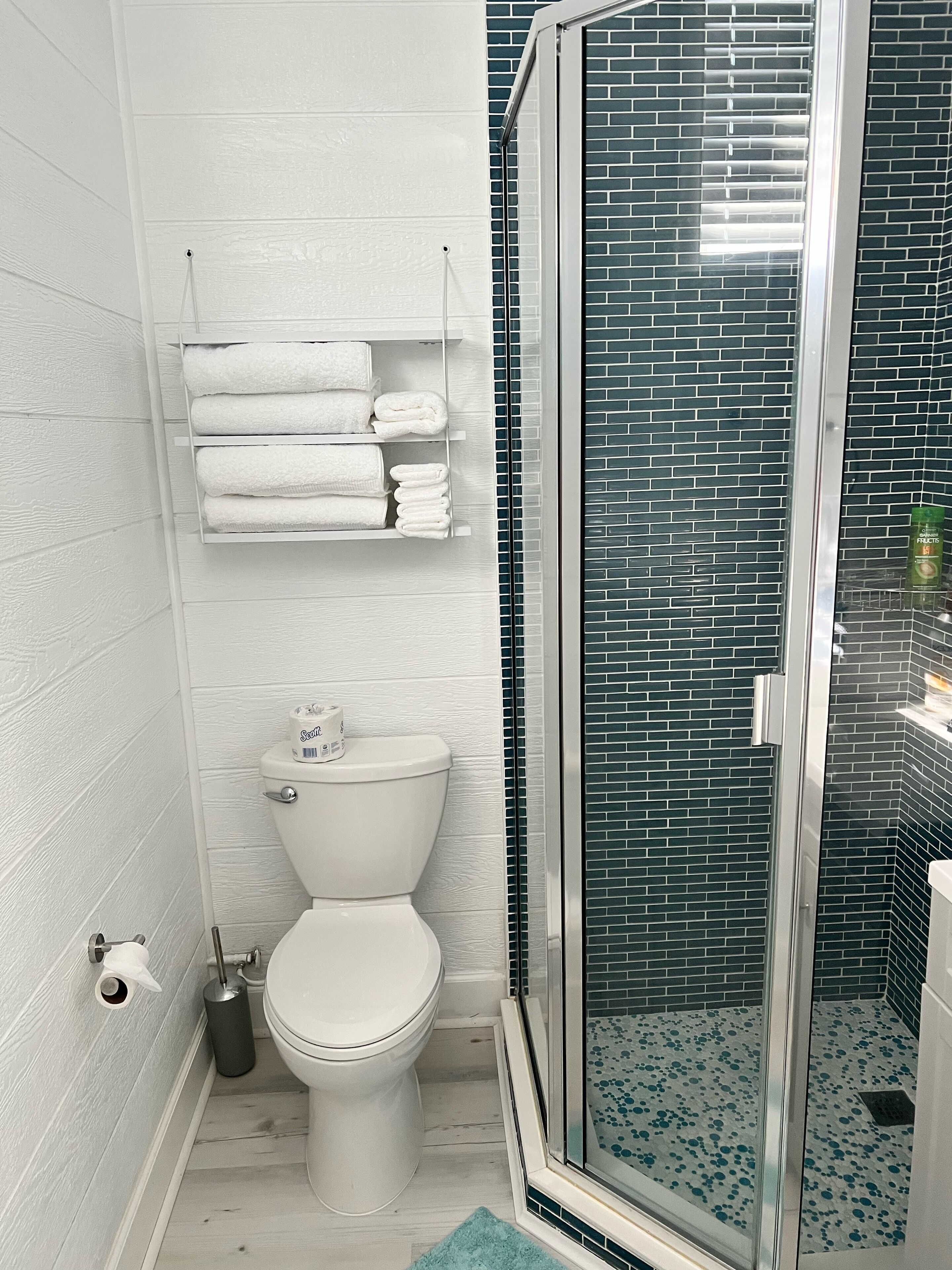 Een badkamer met een wit toilet, een douchecabine van glas en een handdoekrek met netjes opgevouwen handdoeken.