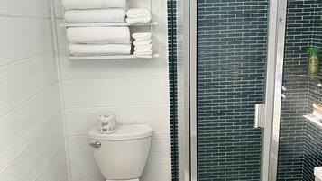 Een badkamer met een wit toilet, een douchecabine van glas en een handdoekrek met netjes opgevouwen handdoeken.