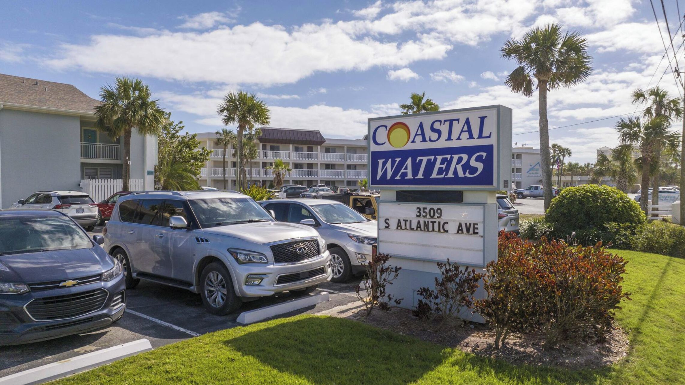 A sign for Coastal Waters hotel with a parking lot in front.