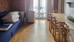 Une pièce chaleureuse avec un plafond en bois, un mur en briques, un canapé bleu, une table à manger en bois avec des chaises, et une grande fenêtre avec des rideaux.