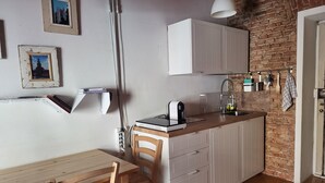 Une cuisine compacte avec des meubles blancs, une table à manger en bois et un mur en briques.