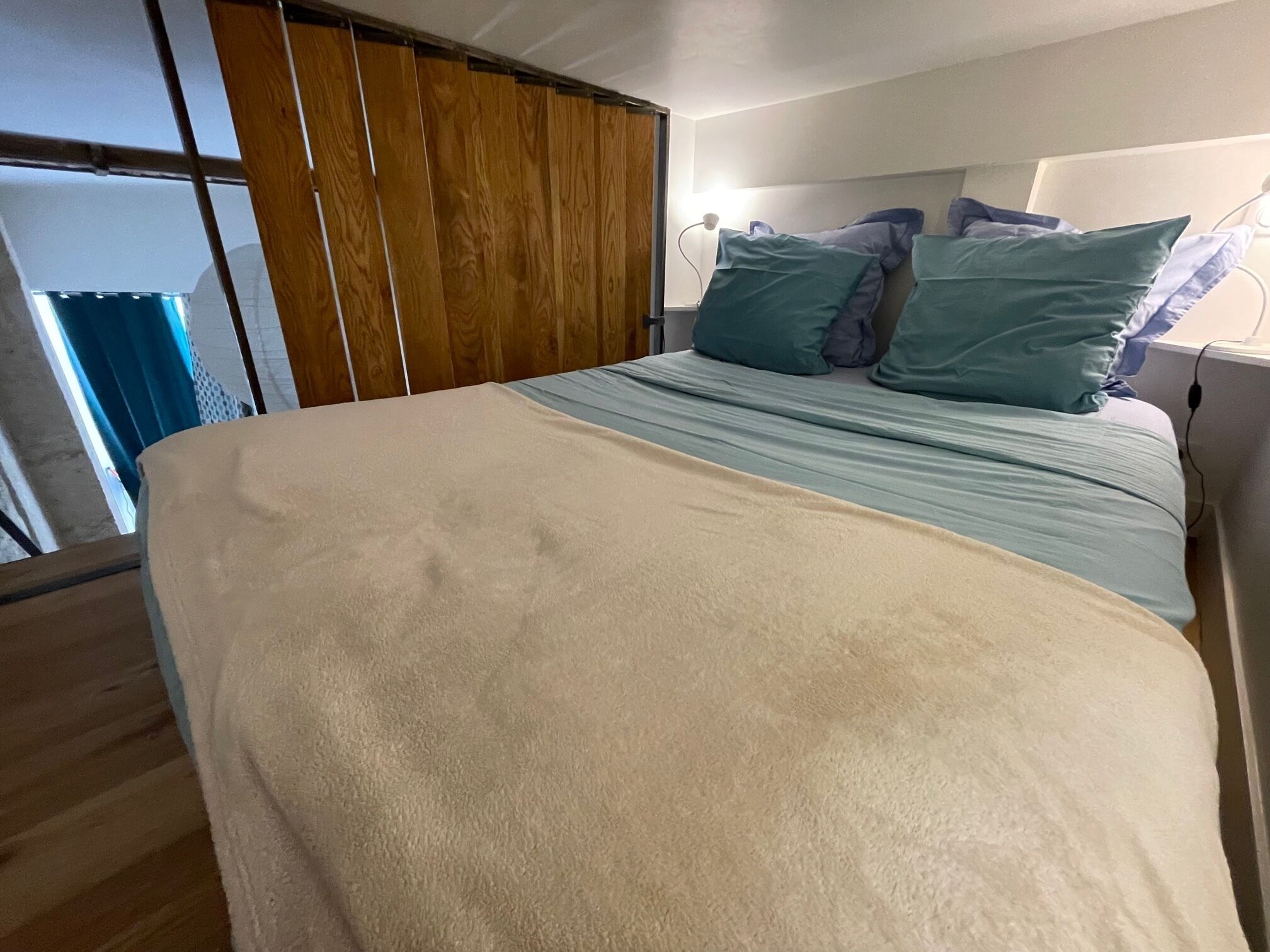 A bedroom with a bed, wooden panel curtains, and a nightstand with a lamp.