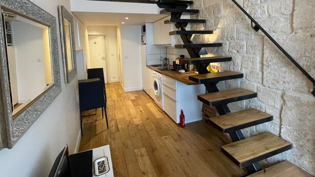 Une cuisine moderne dotée d’un four encastré, un coin repas avec une chaise noire et un escalier avec un mur en pierre.