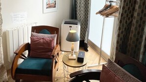 Un salon chaleureux avec un plancher en bois, un radiateur, une table avec une lampe et un fauteuil avec un coussin.