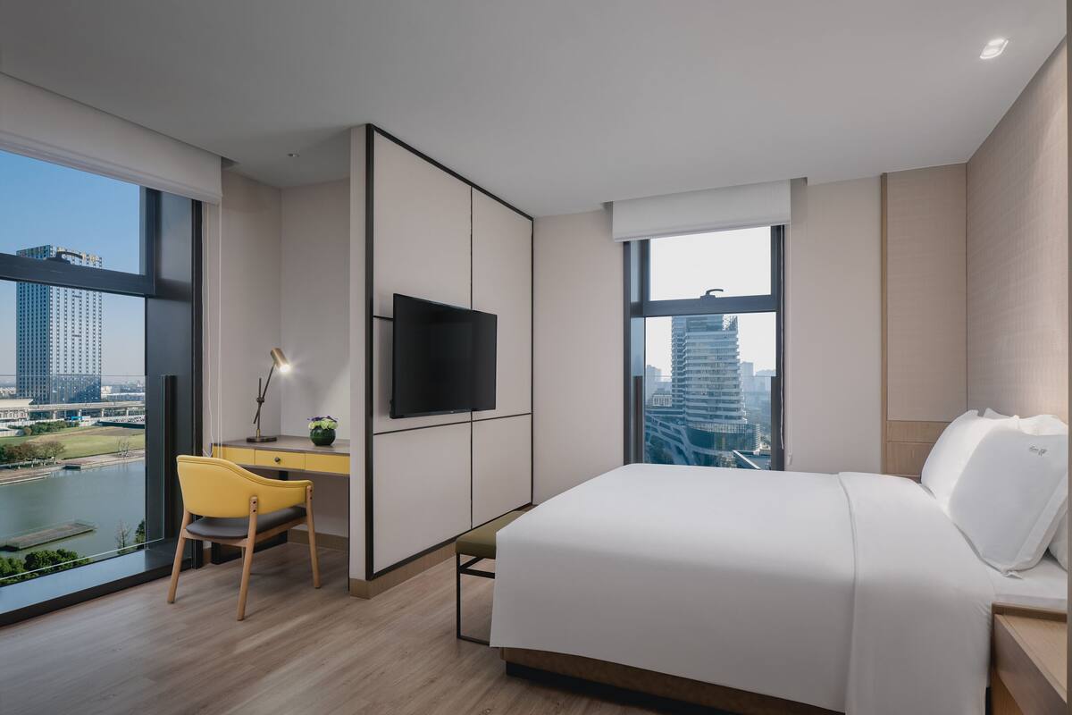 Habitación de hotel moderna con una cama grande, un escritorio con silla, televisión y vistas a un paisaje urbano.