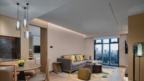 A modern living room with a dining area, a grey sofa, and a large window offering a city view. - Holiday Inn Hotel and Suites Kunshan Huaqiao by IHG (Suzhou)