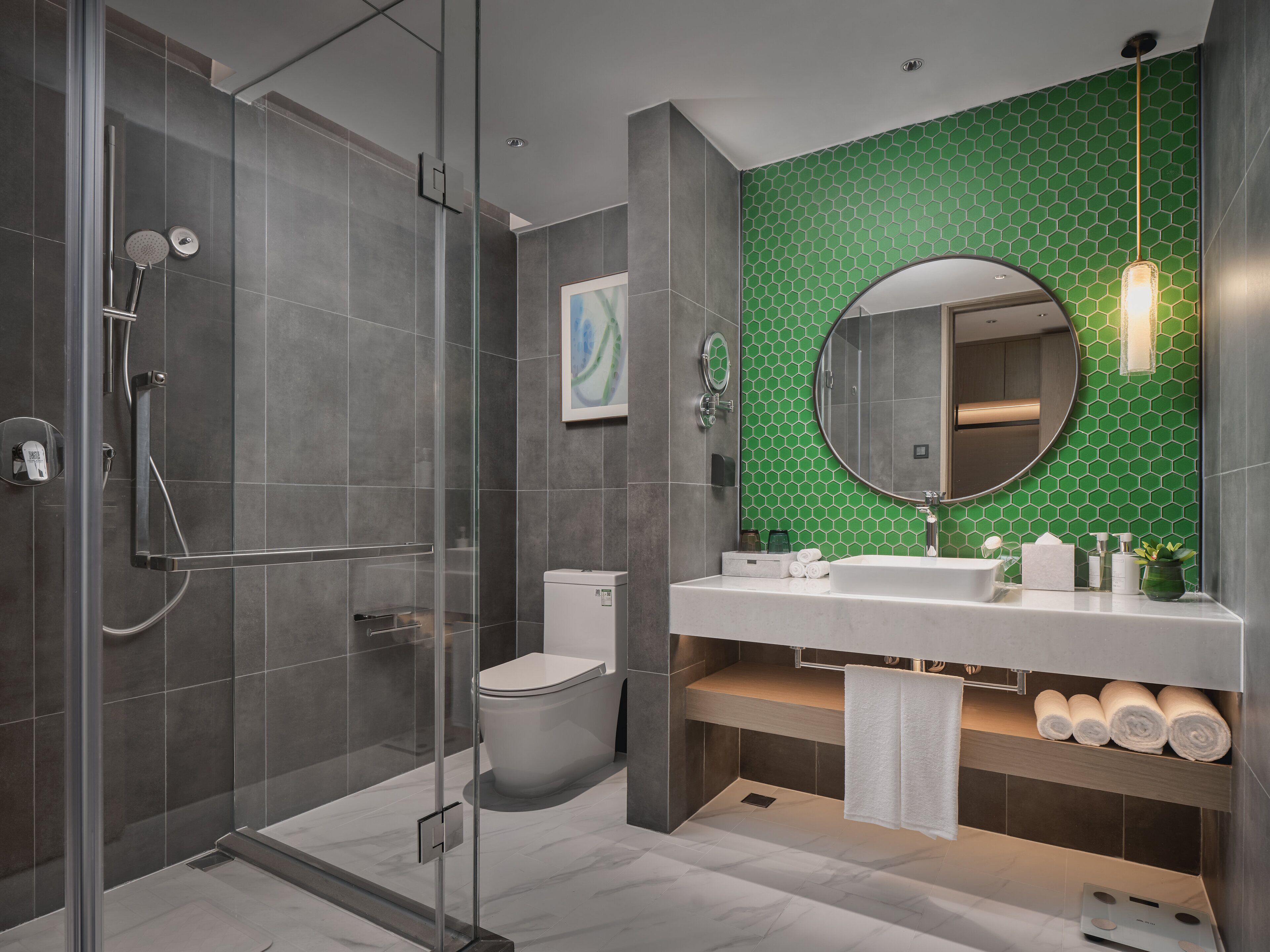 A modern bathroom with a glass-enclosed shower, a toilet, and a vanity with a green hexagonal tile backsplash.
