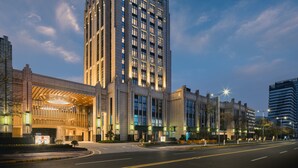 A tall hotel with a prominent 'Holiday Inn & Suites' sign, featuring a modern facade with large windows and a well-lit entrance. - Holiday Inn Hotel and Suites Kunshan Huaqiao by IHG (Suzhou)