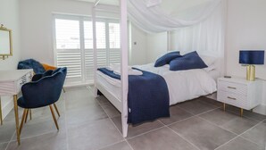 A bedroom with a canopy bed, a desk with a chair, a bedside table with a lamp, and a window with blinds. - 30 Cliff Edge (Newquay)