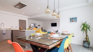 A modern kitchen and dining area with a large wooden table, colorful chairs, and pendant lighting. - 30 Cliff Edge (Newquay)