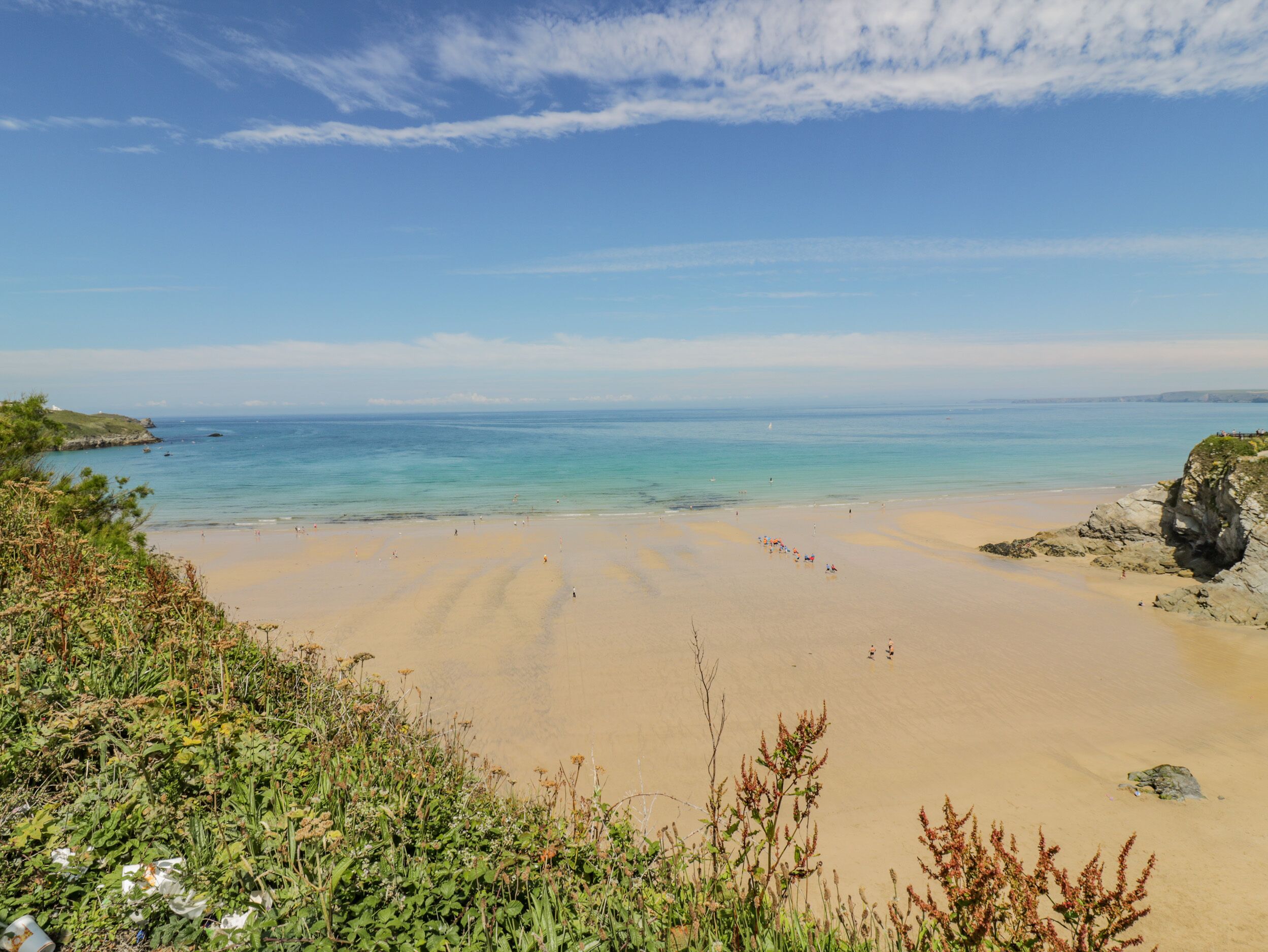 Ein Strand mit klarem, blauem Wasser, Sandküste und Felsformationen.