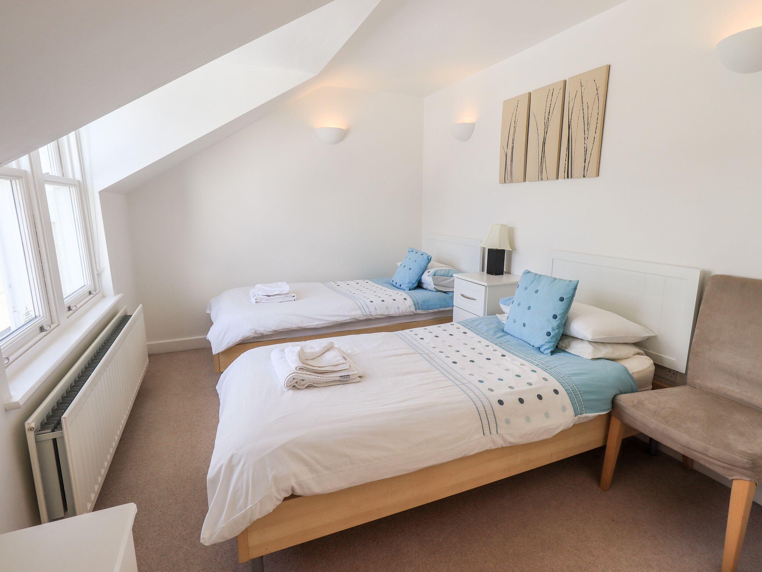 A bedroom with two beds, a nightstand, a chair, and a radiator.