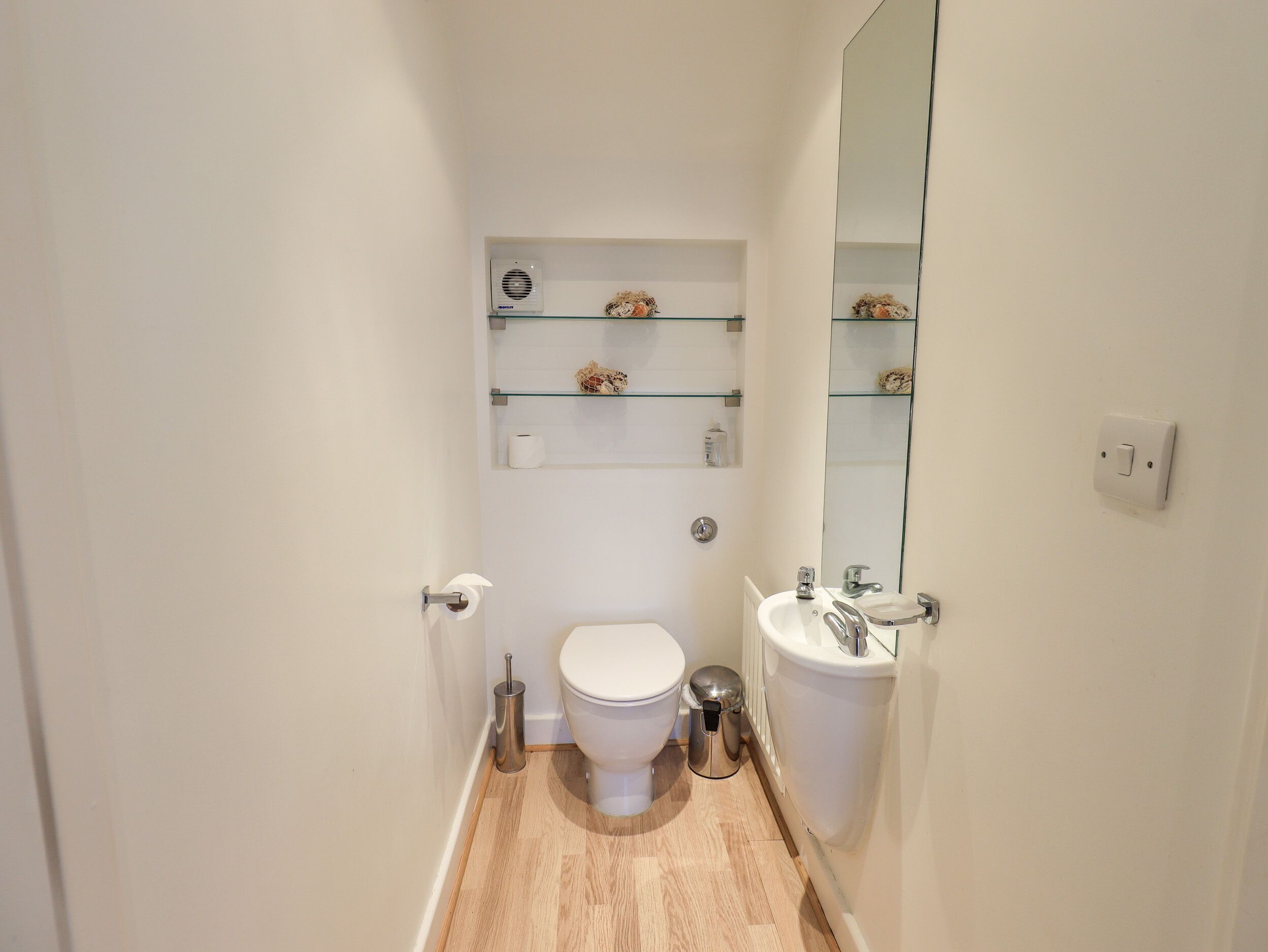 A small, modern bathroom with a toilet, sink, and glass shelves.