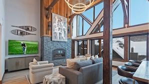 A spacious living room with a large flat-screen TV, a fireplace, and a high ceiling with wooden beams. - The Lodge at Mountain Village | Stunning Ski-In/Out Presidential Penthouse | A Nestique Property (Park City)