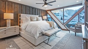 A bedroom with a large bed, a bench, a nightstand, and a view of a snowy mountain. - The Lodge at Mountain Village | Stunning Ski-In/Out Presidential Penthouse | A Nestique Property (Park City)