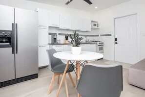 A modern kitchen with white cabinets, a stainless steel refrigerator, a microwave, and a stove. There is a round dining table with two chairs and a potted plant. - Stylish well decorated one bedroom apartment (Miami)