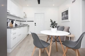 A modern kitchen with white cabinets, a white dining table with four chairs, and a potted plant. - Stylish well decorated one bedroom apartment (Miami)