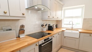 A modern kitchen with white cabinets, a wooden countertop, a built-in oven, a stovetop, and a window with a sink. - The Old Store, 2 Alpine Terrace (Richmond)