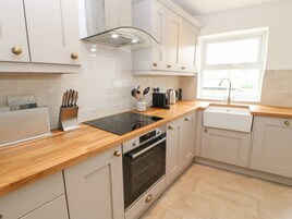 A modern kitchen with white cabinets, a wooden countertop, a built-in oven, a stovetop, and a window with a sink.