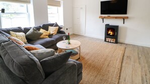 A modern living room with a sofa, a fireplace, a television, and a window with blinds. - The Old Store, 2 Alpine Terrace (Richmond)