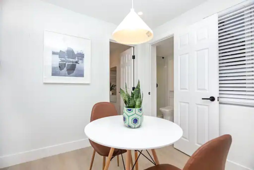 Un coin repas avec une table ronde, des chaises, un luminaire suspendu, une plante en pot et un tableau encadré au mur.