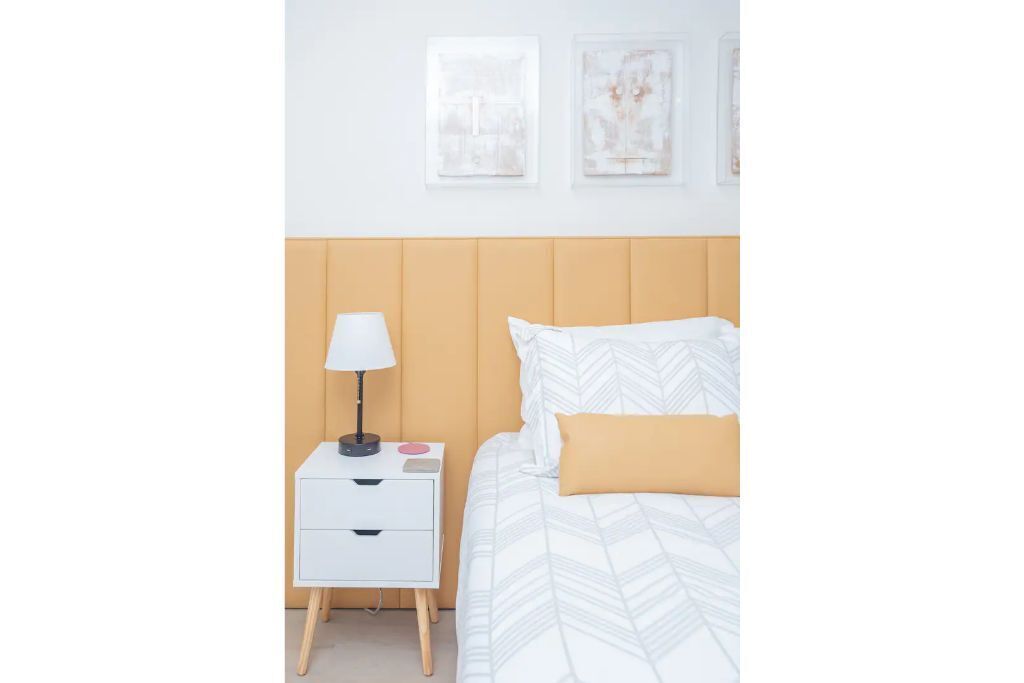 Une chambre à coucher bien rangée, avec un lit, une table de chevet dotée d’une lampe et deux tableaux encadrés accrochés au mur.