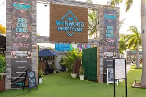 An outdoor entrance to Wynwood Market Place with a wooden archway, banners for Tres Cero Cinco, and a live music event.