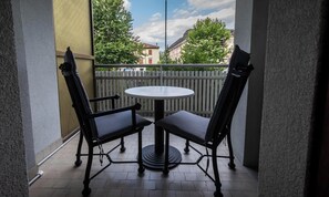 En balkon med to stole og et bord, et hvidt gelænder og bygninger i baggrunden.