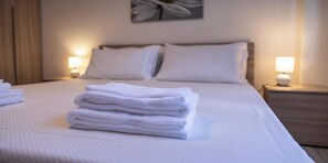 Ein ordentlich bezogenes Bett mit weißen Laken, zwei Nachttischlampen und einem an der Wand hängenden Kunstwerk.