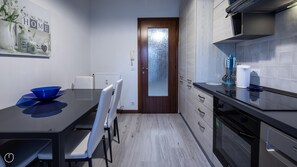 Et moderne køkken med spiseplads, med dør i træ, rustfrie stålapparater og hvid flis bag komfuret.