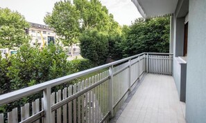 Ein Balkon mit Fliesenboden, Metallgeländer und Blick auf Bäume und Gebäude.