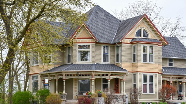 A large, two-story house with a prominent front porch, multiple windows, and a stone foundation. - Magnificently restored, charming, 8+ Bed-Victorian on a beautiful 1.5 acres. (Waukesha)