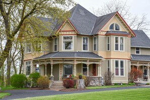Une grande maison à deux étages, dotée d’un porche avant imposant, de nombreuses fenêtres et de fondations en pierre.