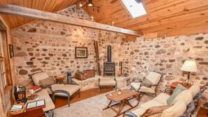 A cozy room with stone walls, wooden ceiling beams, a fireplace, and comfortable seating. - Magnificently restored, charming, 8+ Bed-Victorian on a beautiful 1.5 acres. (Waukesha)