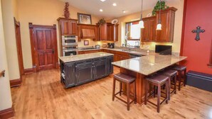 A kitchen with wooden cabinets, a granite countertop, and a central island with bar stools. - Magnificently restored, charming, 8+ Bed-Victorian on a beautiful 1.5 acres. (Waukesha)