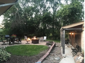 An outdoor patio with a fire pit, seating, and a covered area with chairs. - Magnificently restored, charming, 8+ Bed-Victorian on a beautiful 1.5 acres. (Waukesha)